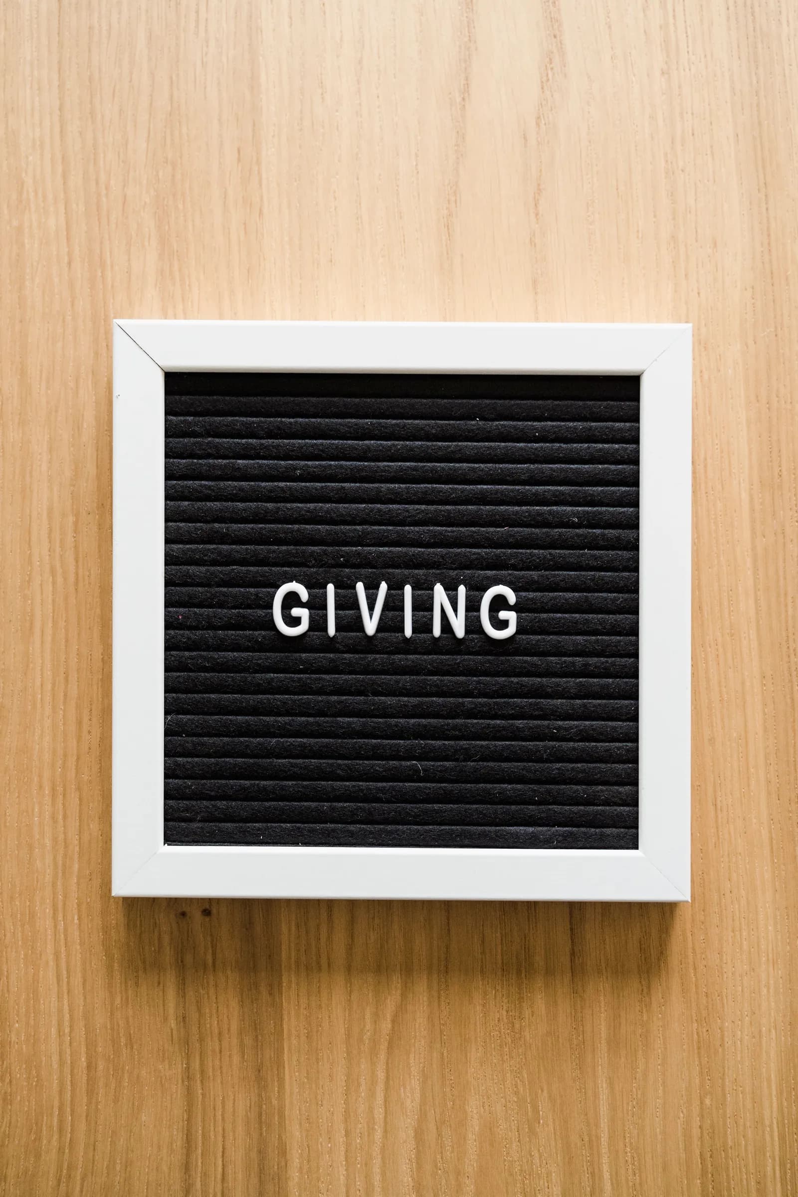 A framed giving sign on a wooden background.